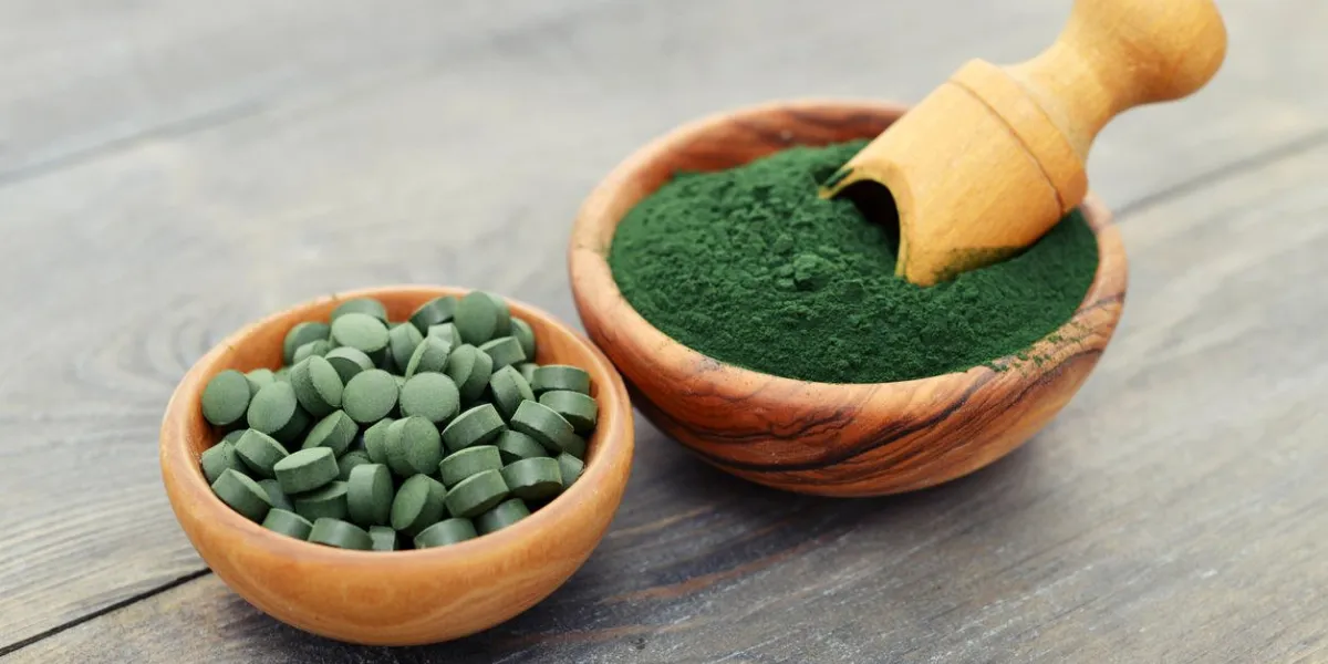 spiruline moulue et spiruline en pilules sur fond en bois noir