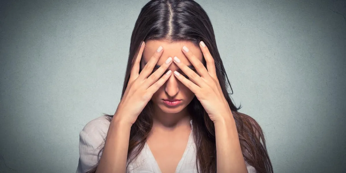 closeup portrait triste jeune belle femme avec l'expression du visage stressé inquiet couvrant le visage avec les mains regardant vers le bas