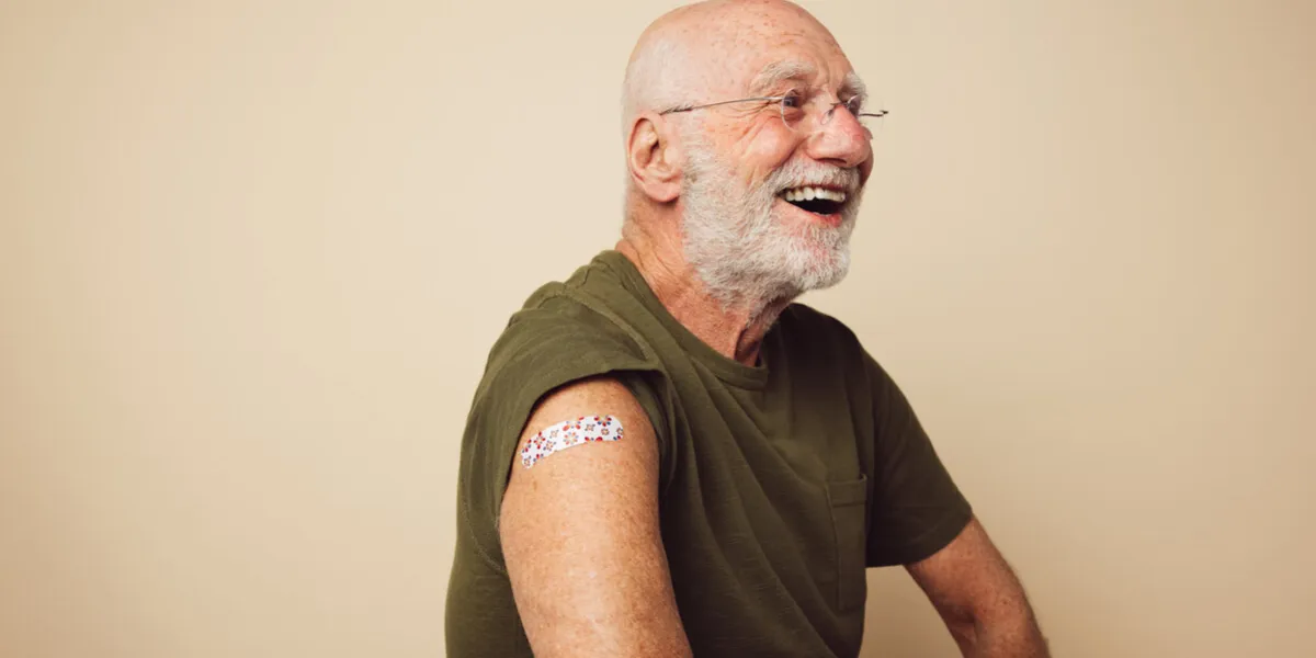 portrait of senior man with bandage on arm after getting vaccine elderly man laughing against brown background after receiving immunity vaccination
