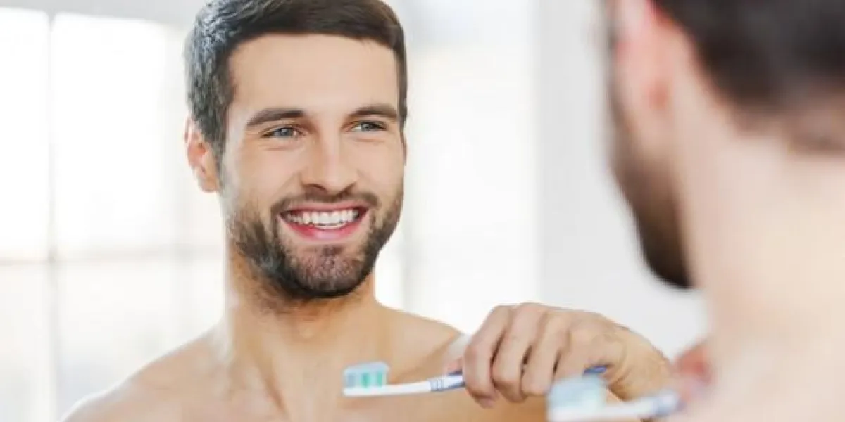bonjour arrière vue de beau jeune homme barbe tenant la brosse à dents et souriant tout en se tenant debout contre un miroir