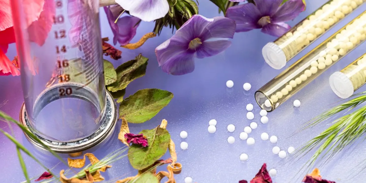 petits tubes en verre avec globules homéopathiques, seringue et fleurs