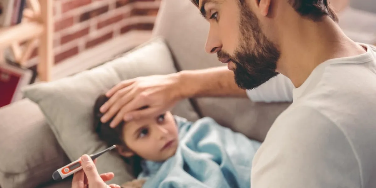 petite fille malade couverte de couverture est couchée sur le canapé pendant que son père prend sa température