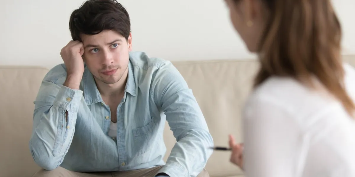 young serious man sitting on the couch listening attentively to advices of psychologist, doctor or psychotherapist, discussing medical test results, explaining diagnosis, treatment methods