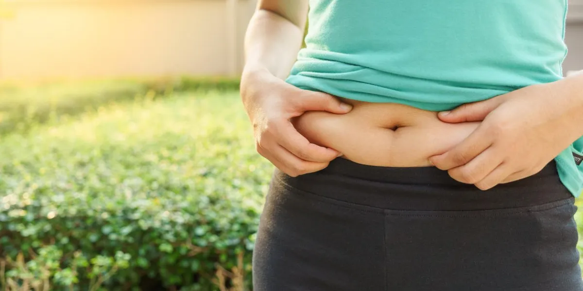 chubby woman hand holding her own belly fat at outdoor under the sunlight