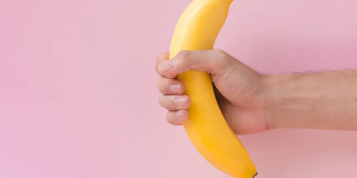 male hand holding a banana isolated on pink background