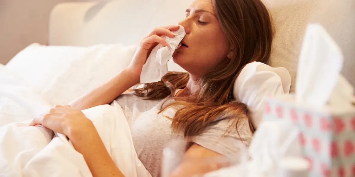woman suffering from cold lying in bed with tissue