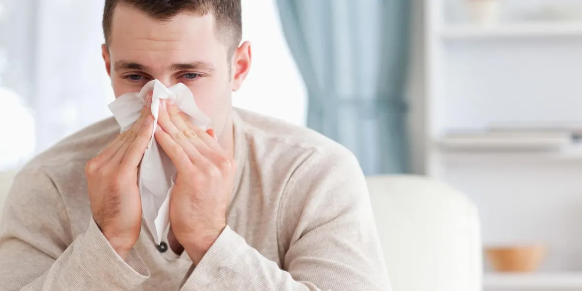 man blowing his nose in his living room