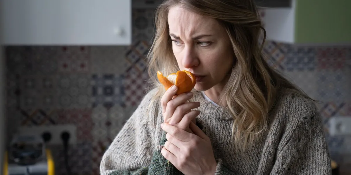 woman trying to sense smell of tangerine orange, has symptoms of covid-19 corona virus infection