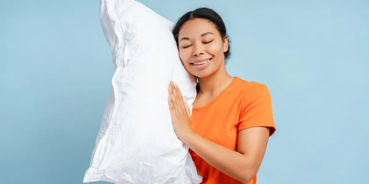 happy african american woman sleeping, holding white pillow isolated on blue background morning concept stock photo