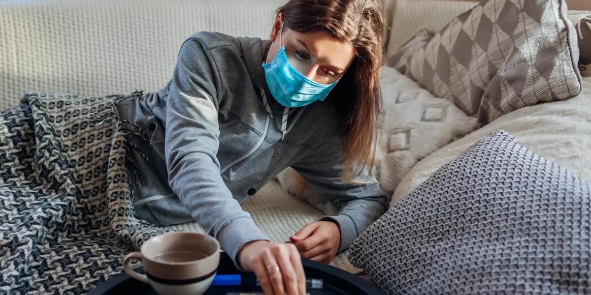 sick woman having fever coronavirus flu or cold ill girl lying in bed wearing protective mask taking pills and water at home healthcare during pandemic quarantine
