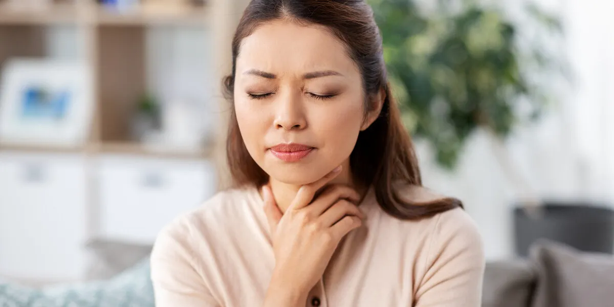 health, cold and people concept - sad sick young asian woman with sore throat at home