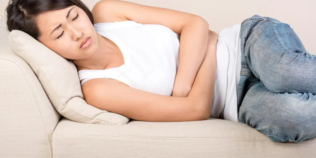 asian young woman is suffering from pain in the stomach, she is lying on the bed