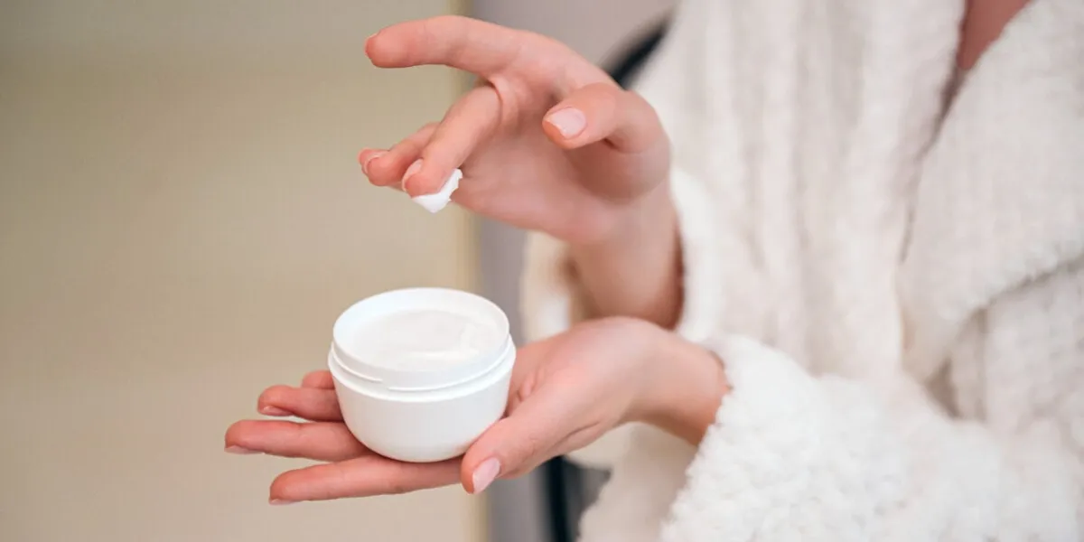 cropped shot of female hand hold white jar with cream woman applying moisturizer products for skin care beauty procedure at home bathroom, closeup view