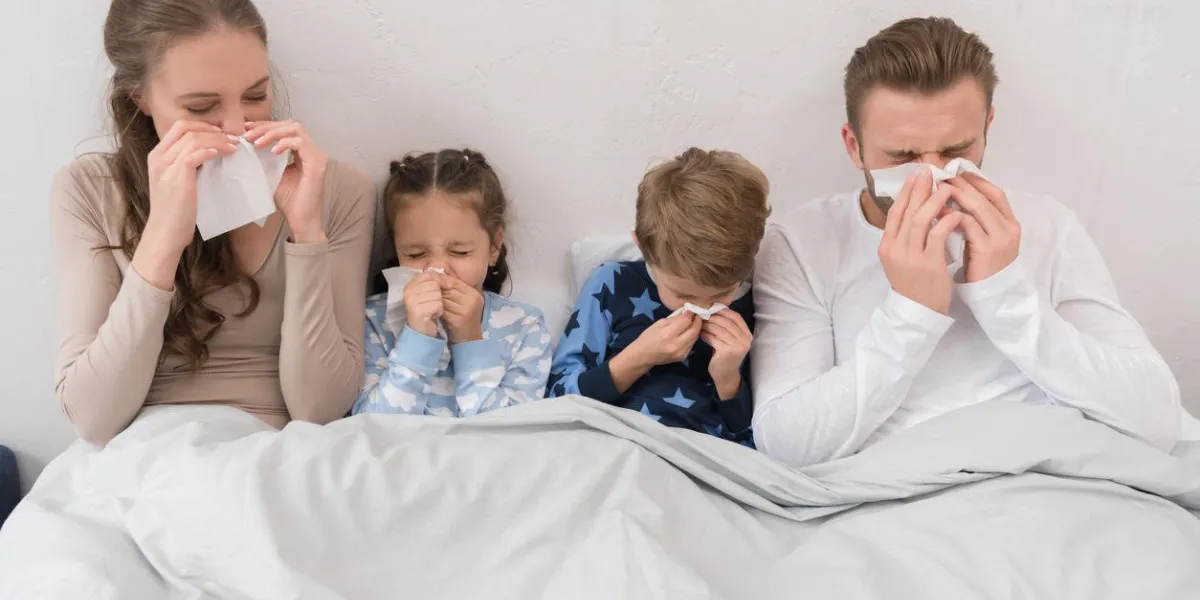 sick parents ans children lying in a bed and blowing noses in napkins