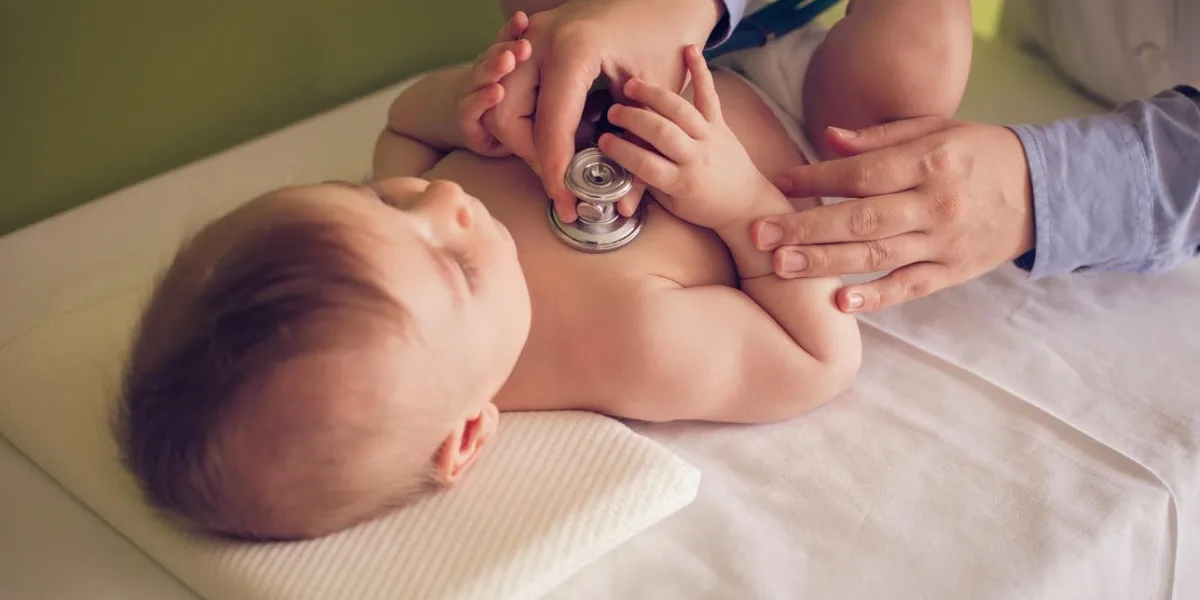 cute baby boy lying down at the doctor office and female doctor listening to his heartbeat with stethoscope