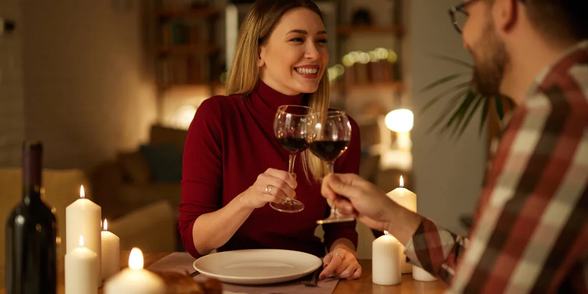 beautiful couple having romantic dinner with candles and red wine at home