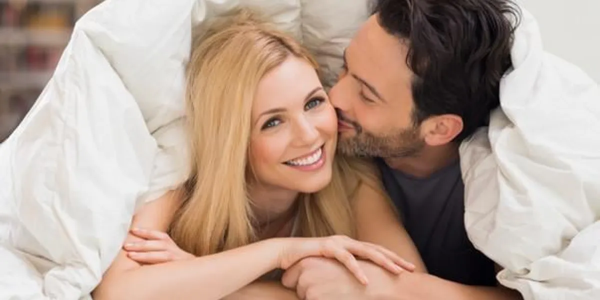 bel homme embrasser femme sur la joue sous une couette dans le lit heureux jeune couple couché confortablement dans leur lit à la maison jeune couple s'amuser couché sur le lit à la maison