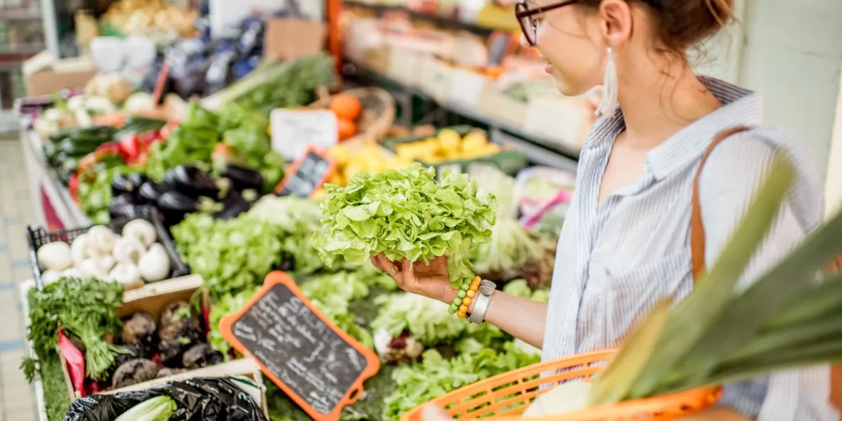 young woman choosing a fresh salad standing with basket at the food market in france