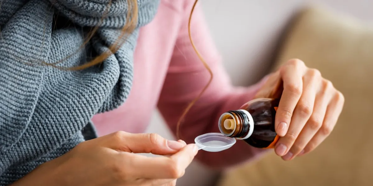 cropped view of ill woman with grey scarf taking cough syrup
