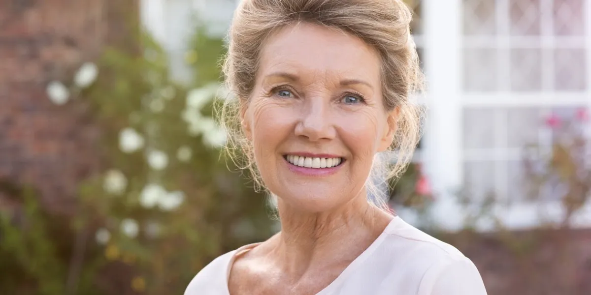 happy senior woman standing outside her house content woman smiling and looking at camera portrait of cheerful old grandmother relaxing outside the house