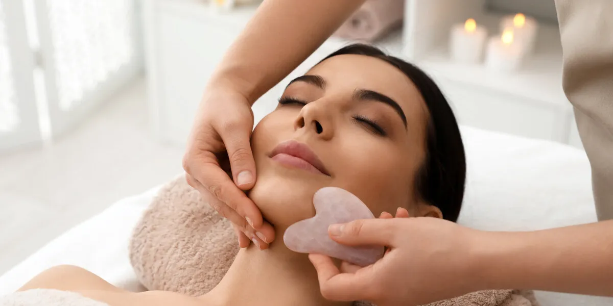 young woman receiving facial massage with gua sha tool in beauty salon