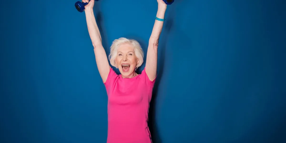 excited senior fitness woman training with dumbbells isolated on blue