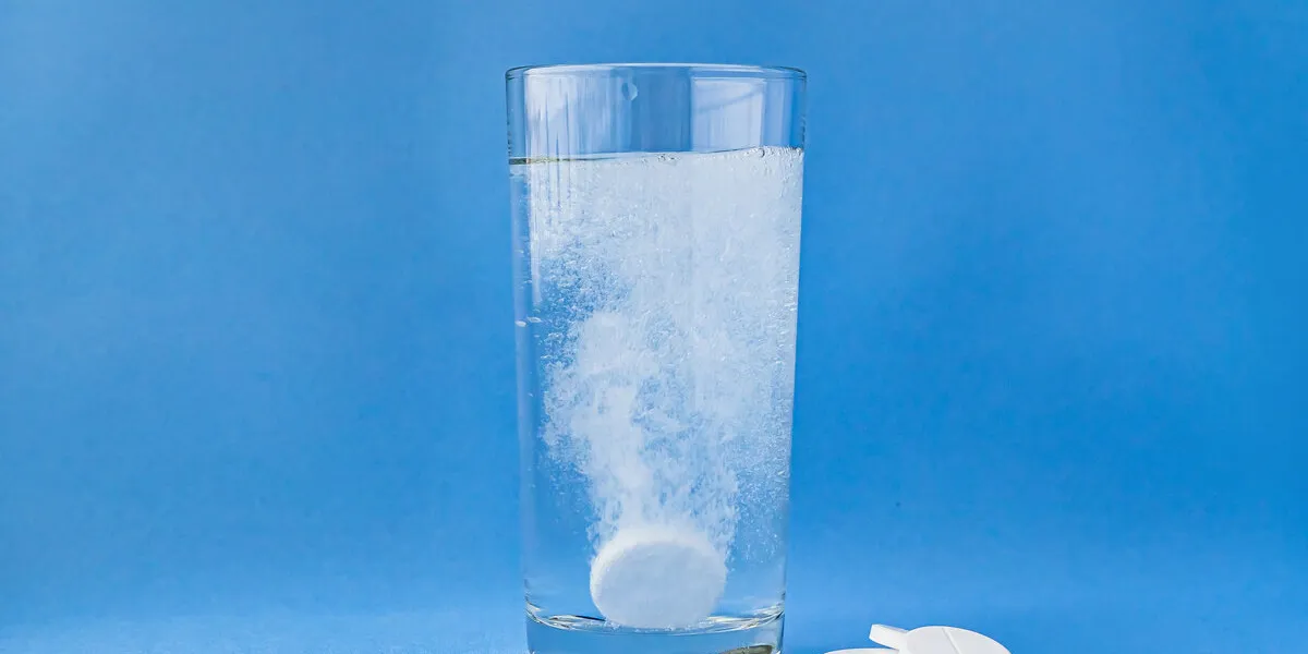 fizzy aspirin in a glass of water on a blue background vertical format and soft focus