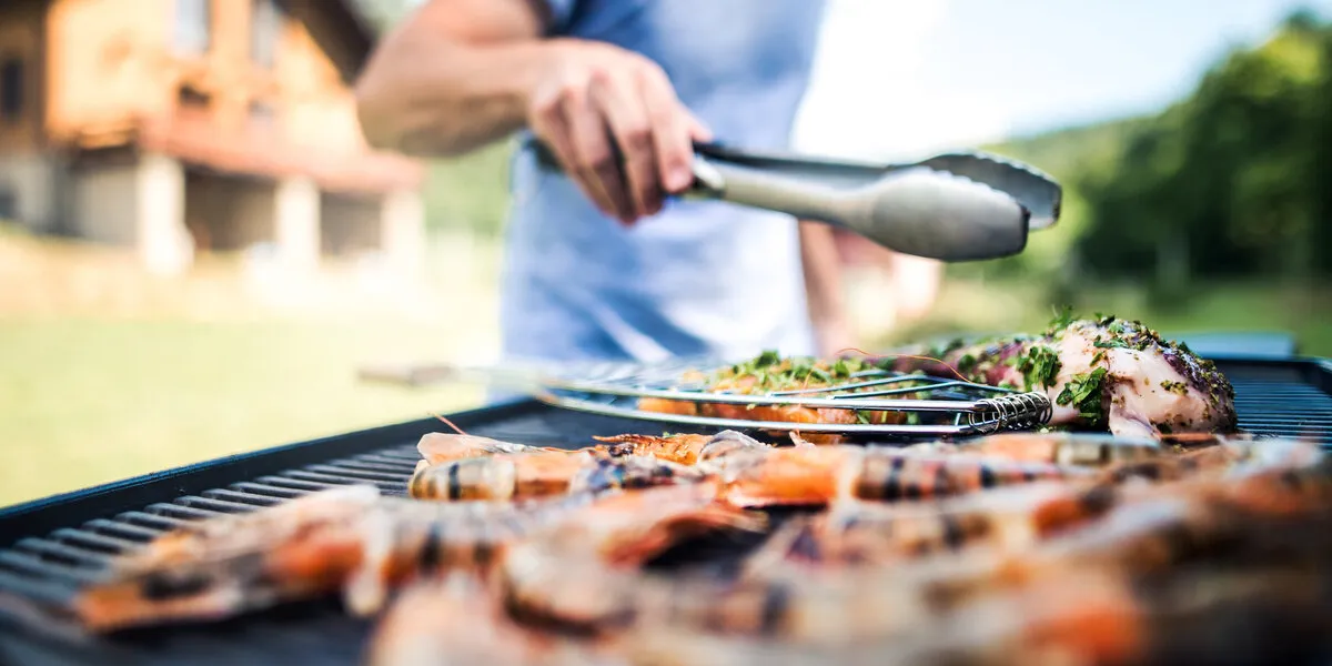 unrecognizable man cooking seafood on a barbecue grill in the backyard on a sunny day