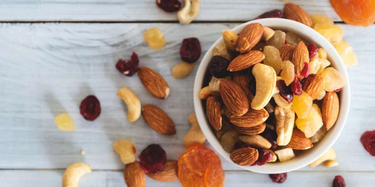 mixed nuts and dried fruit in wooden bowl on wooden table top view walnut, pistachio, almond, hazelnut, cashews, apricot, berry, banana, pineapple, healthy food and snack