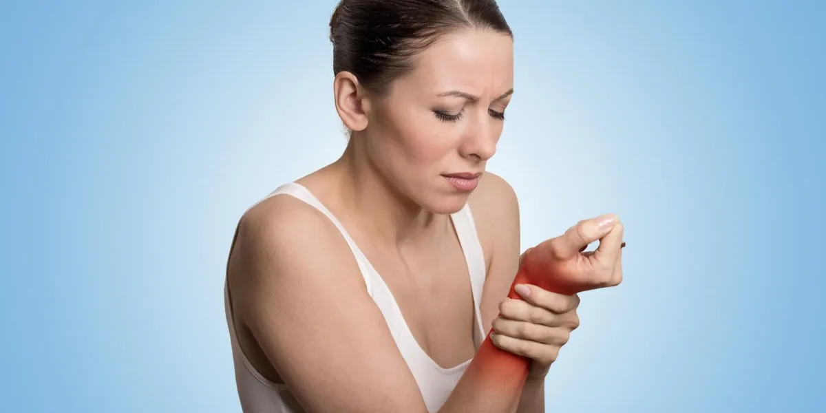 young woman holding her painful wrist over blue background sprain pain location indicated by red spot