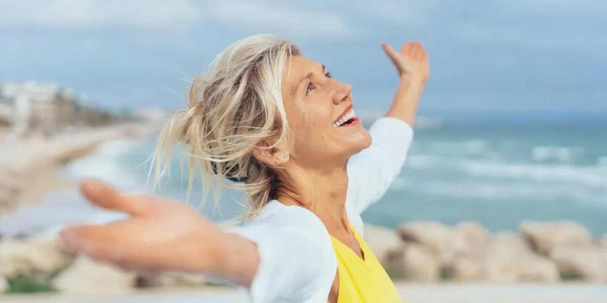 joyful woman enjoying the freedom of the beach standing with open arms and a happy smile looking up towards the sky