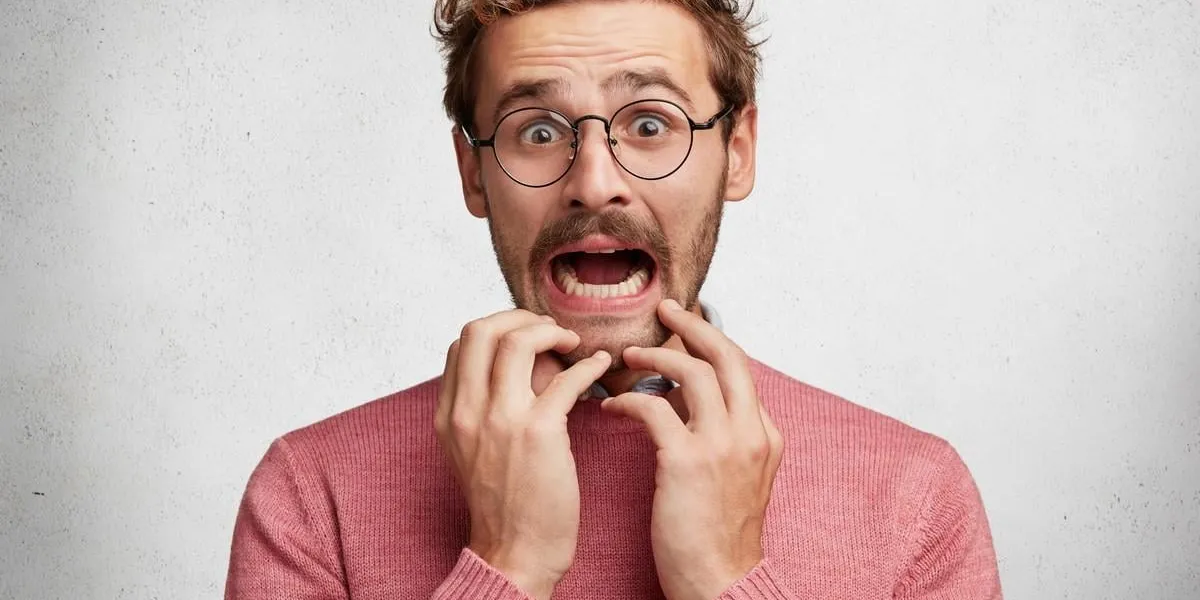 worried scared fashionable man looks with terrified expression, keeps arms on chin, dressed in pink sweater, isolated over white background emotional bearded young guy receives unexpeted news