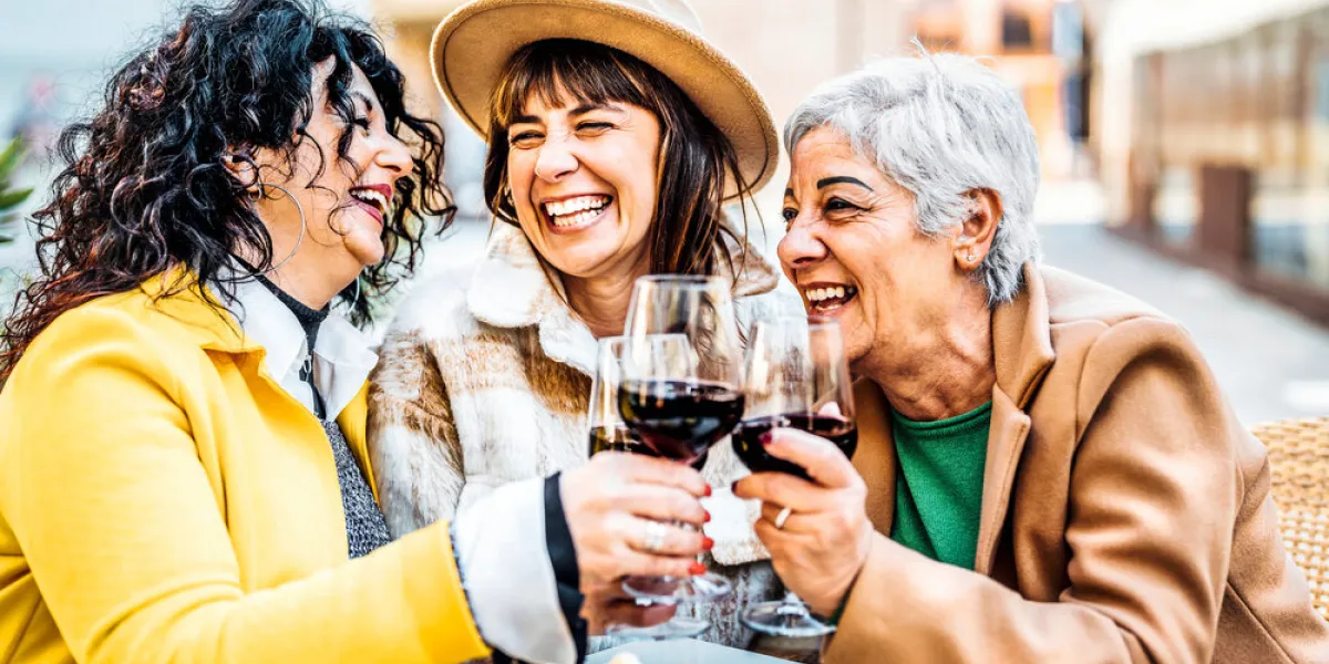 three happy retired female drinking and toasting red wine glasses at bar restaurant - group of happy elderly women having fun in the city - concept about older friends smiling and laughing together