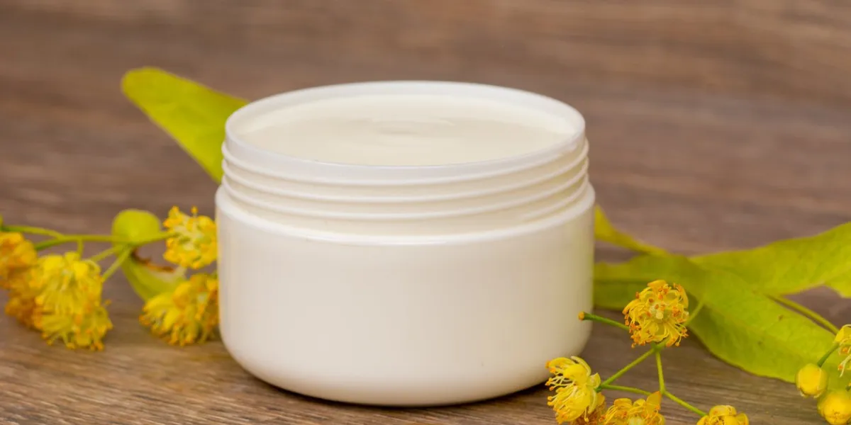 body cream opened plastic jar with chamomile and linden flowers on wooden table