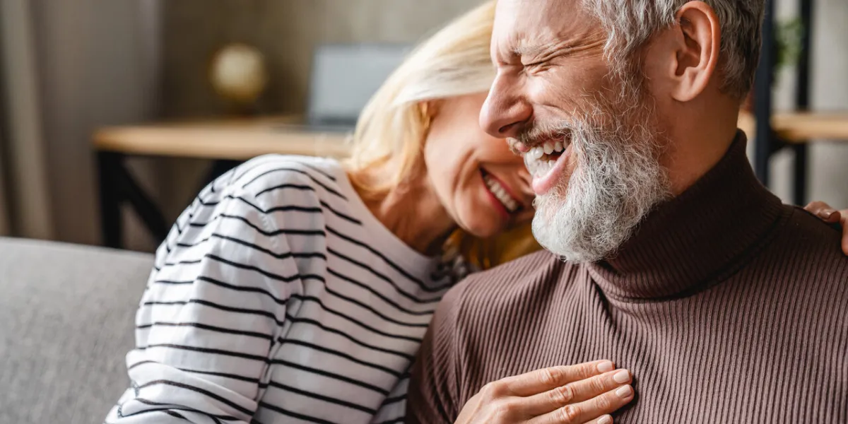 happy laughing middle aged couple bonding while relaxing sitting on sofa