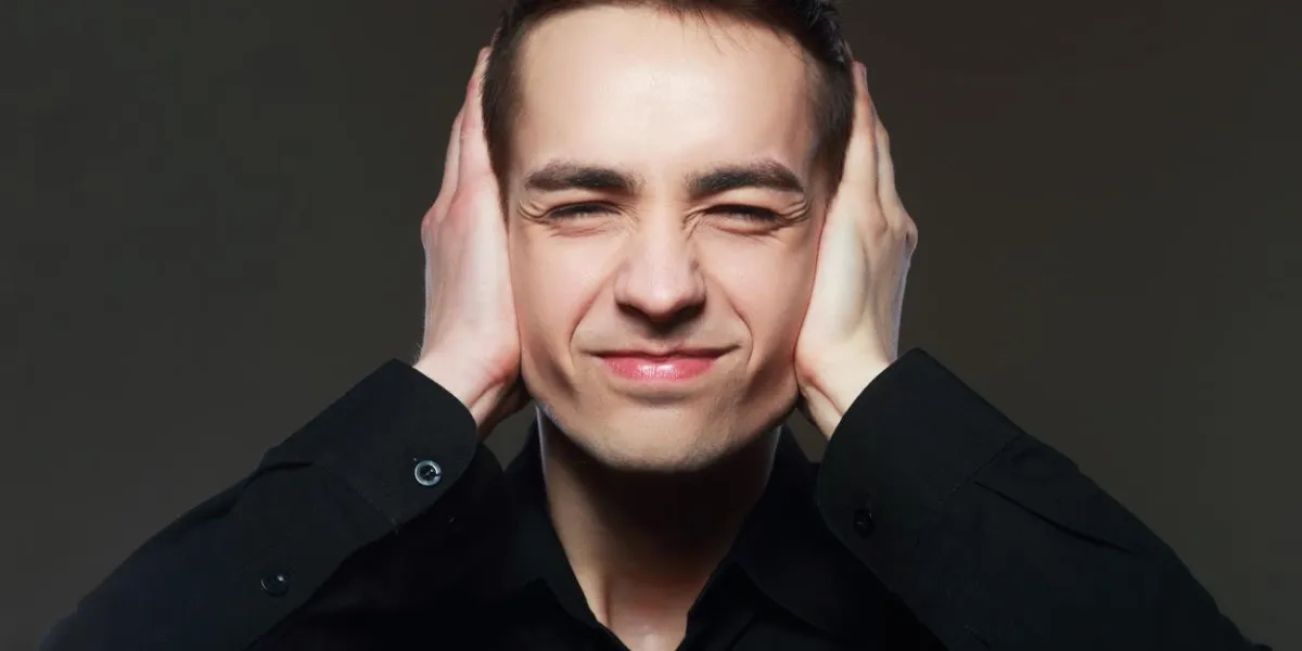 un homme couvre ses oreilles de ses mains souffrant d'un son fort