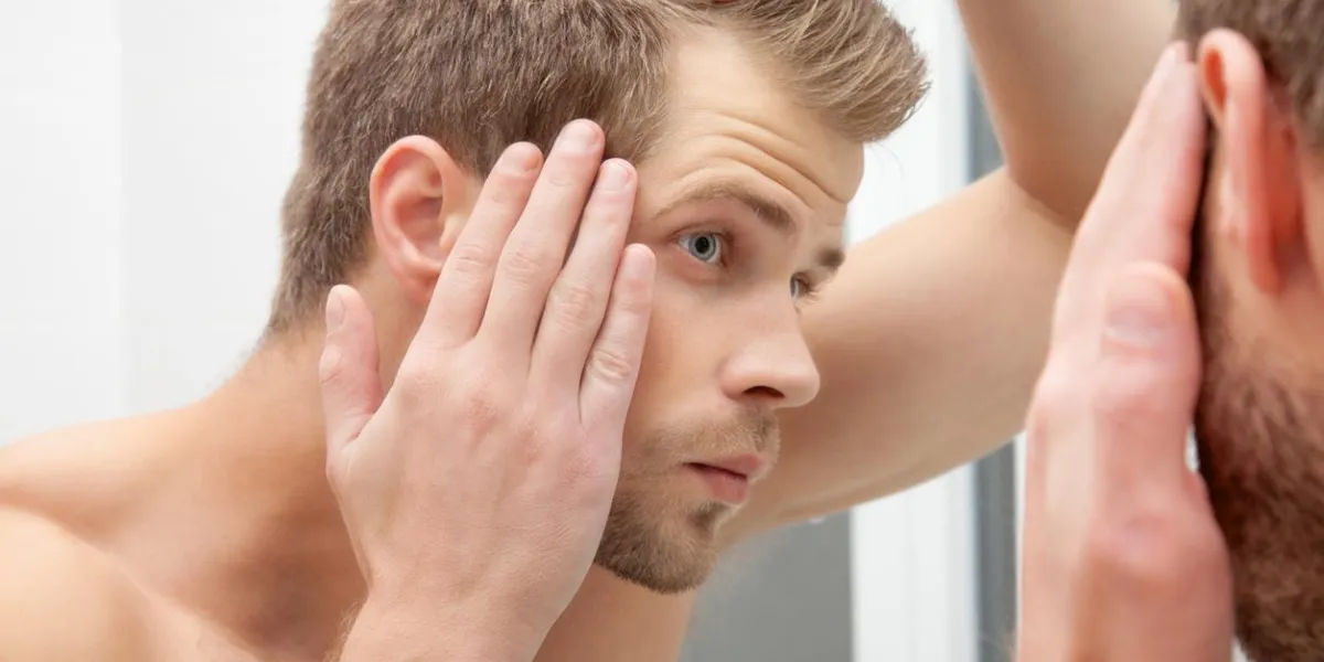 handsome unshaven man looking into the mirror in bathroom