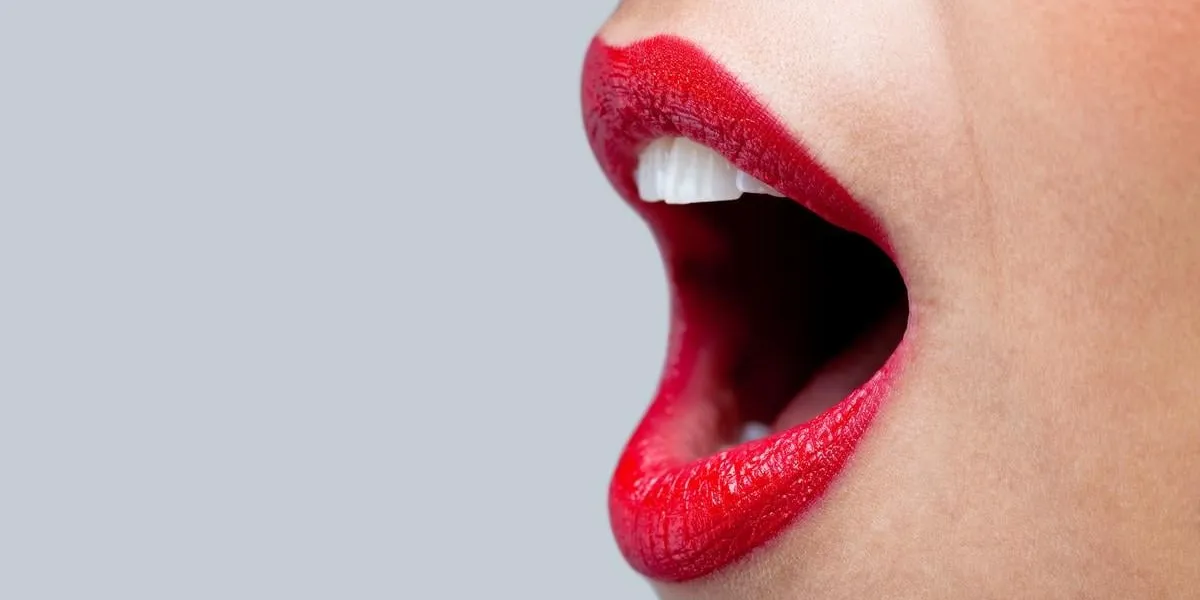 close up of a womans mouth wide open with bright red lipstick on her lips