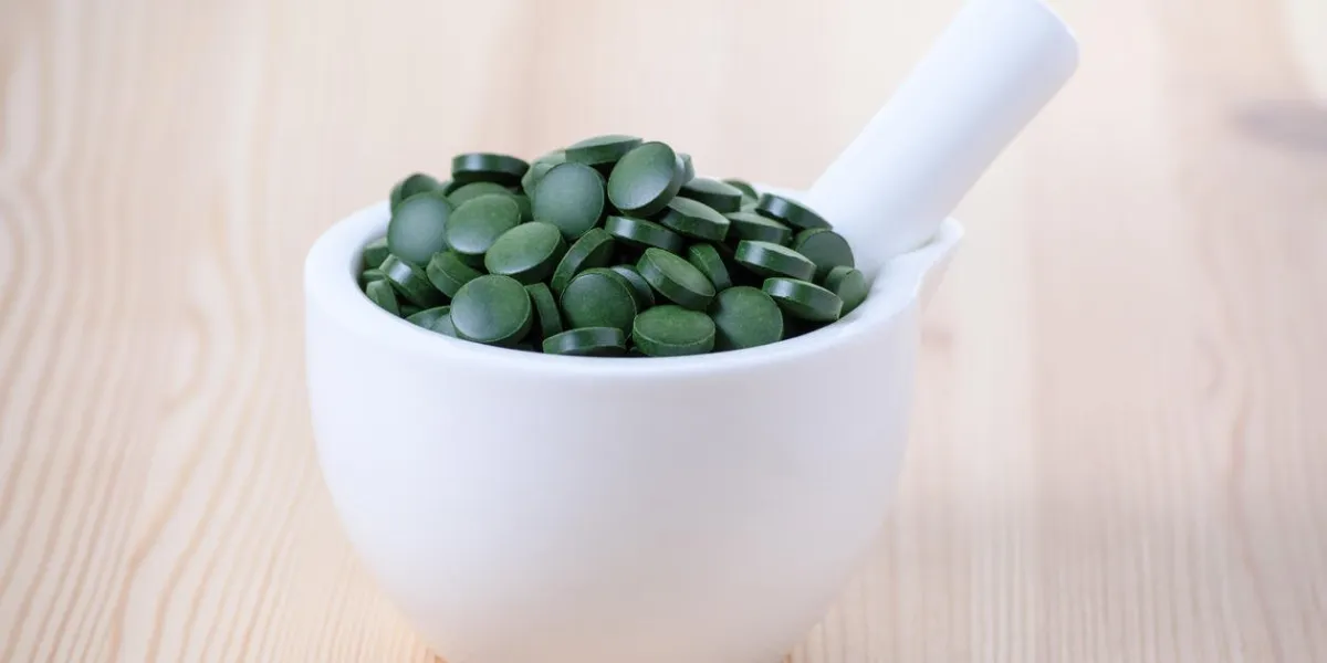 pilules vertes d'algue spiruline chlore dans un bol blanc sur le fond en bois