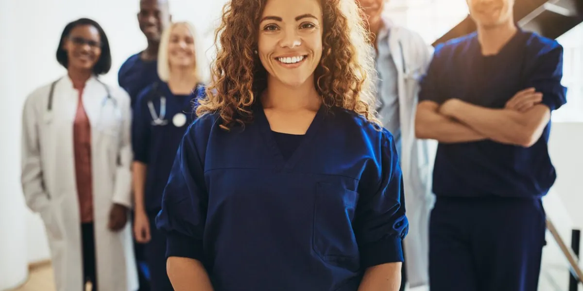 smiling young female doctor standing in a hospital corridor with a diverse group of medical staff standing behind her