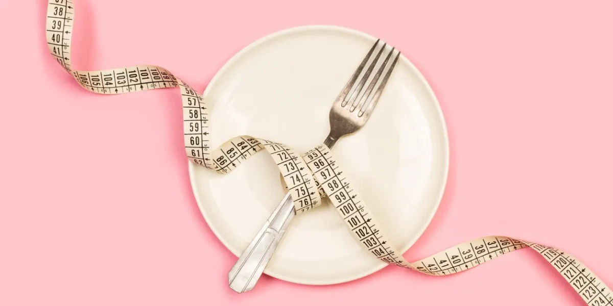 a measuring tape and a fork on a white plate on a pink background in a top view