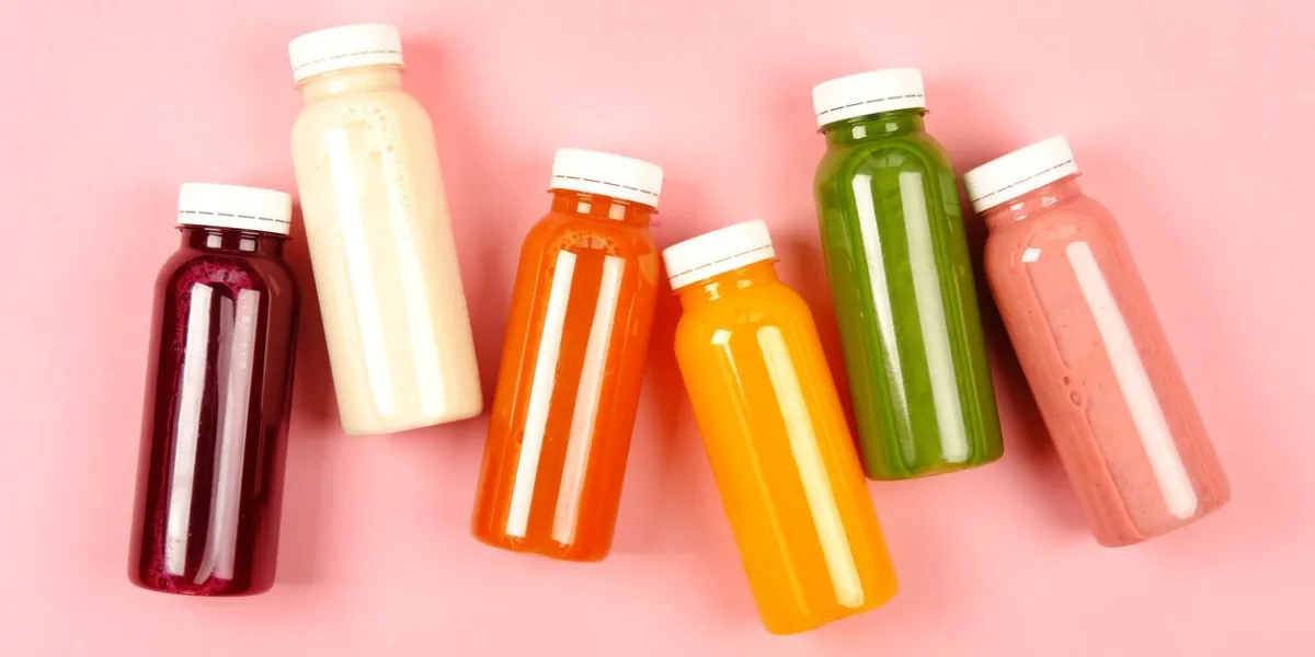 bottles of multicolored smoothies or juices on pink background flat lay style