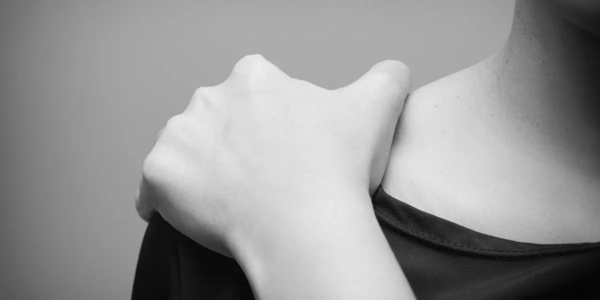 young woman suffering from pain in shoulder, pain in the human body on a gray background- black and white