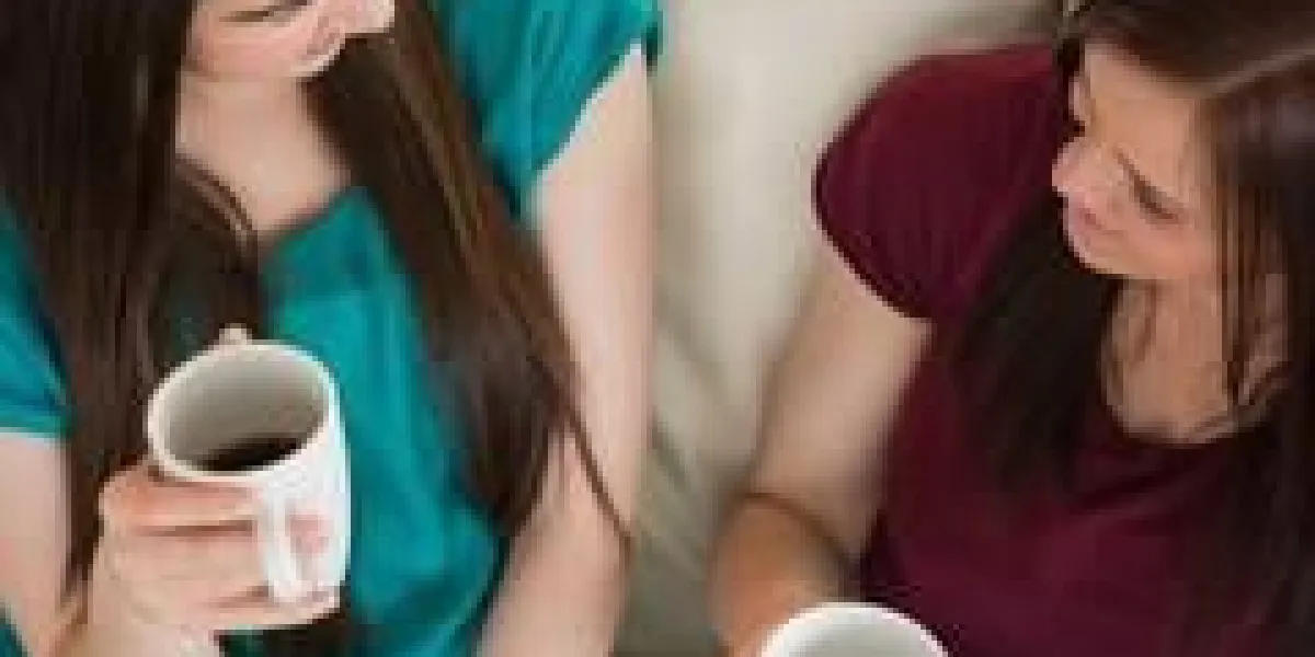 deux amis souriants prenant un café et bavardant sur le canapé à la maison dans le salon