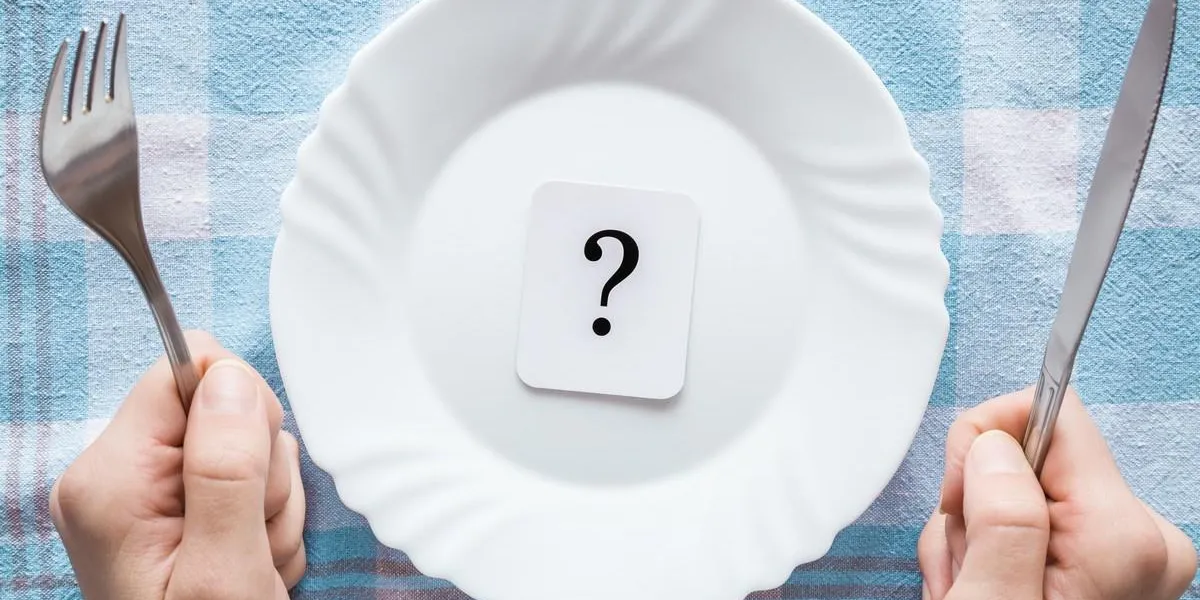 woman's hands holding a fork and knife question mark in the clean, empty, white plate on the tablecloth starving people meal waiting concept top view