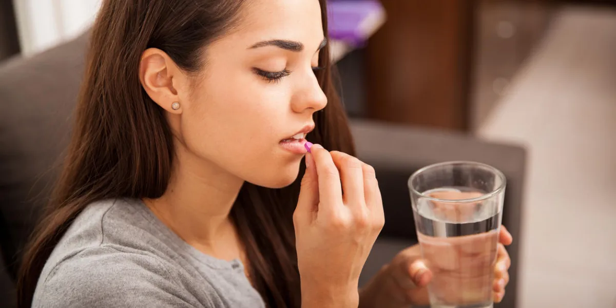 mignonne jeune brune prenant une pilule avec un verre d'eau à la maison