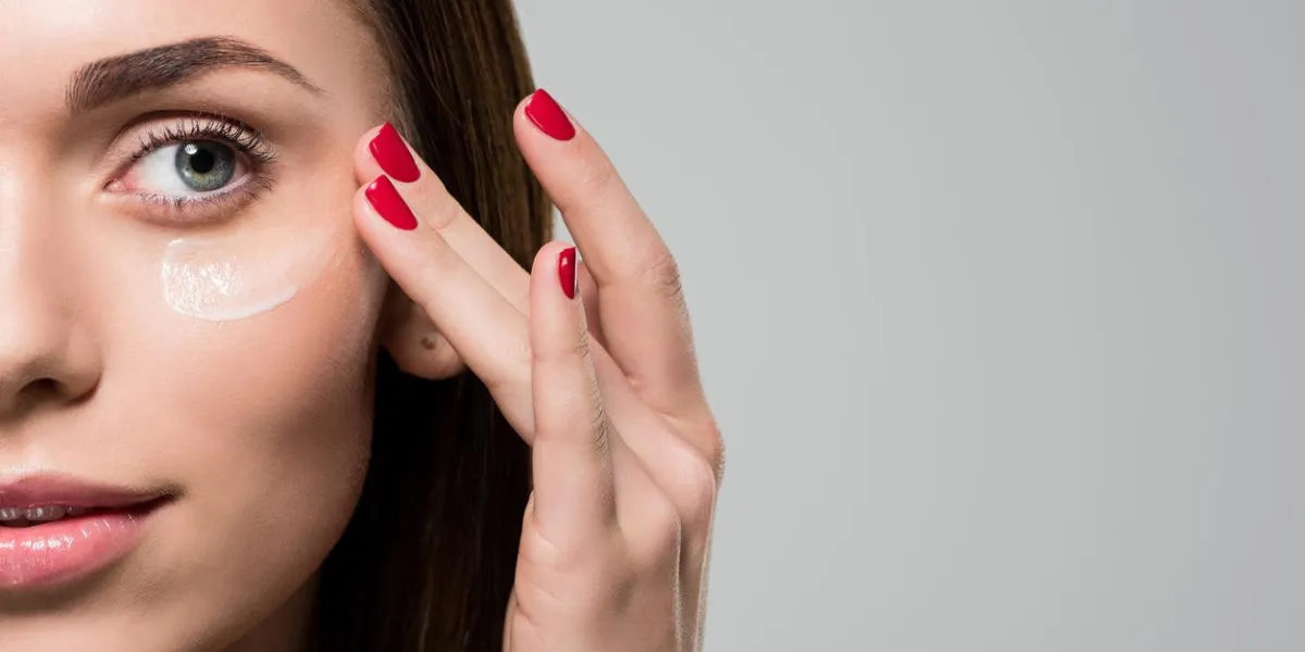 young woman applying facial moisturizing cream isolated on grey
