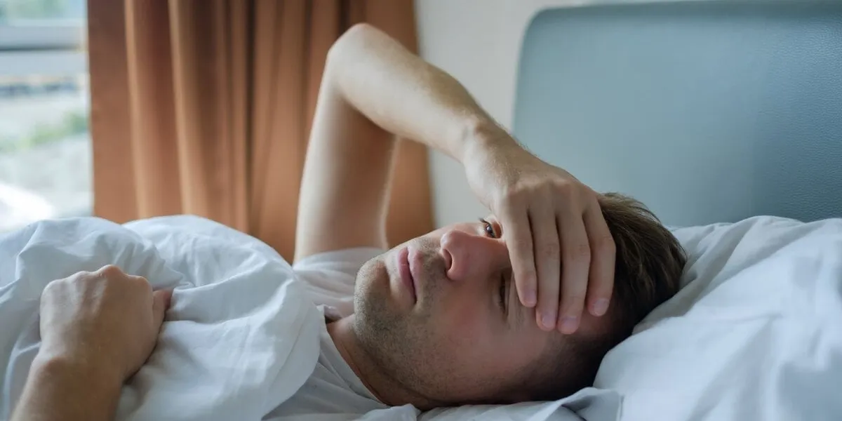 caucasian man lying in bed at home suffering from headache or hangover concept of problem with health