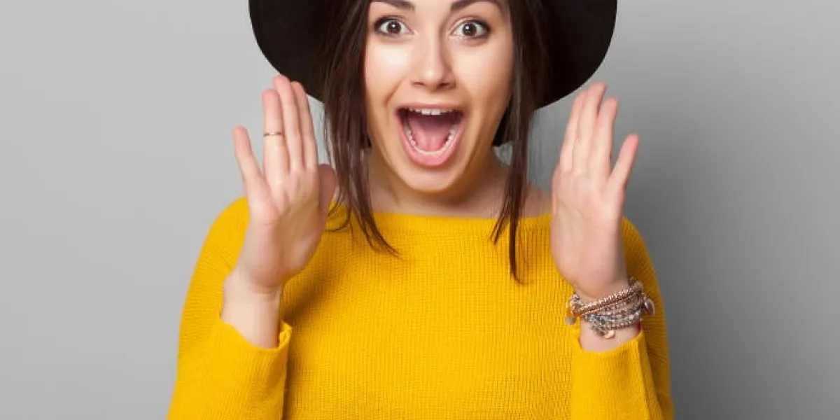 surpris jeune femme portant des vêtements jaunes chauds et élégant chapeau sur fond gris