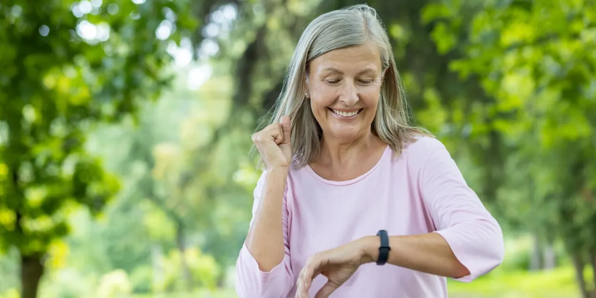 senior gray-haired beautiful woman is running and doing sports in the park and checking the time on the tracker, happy with the result he looks at the smart watch on his wrist